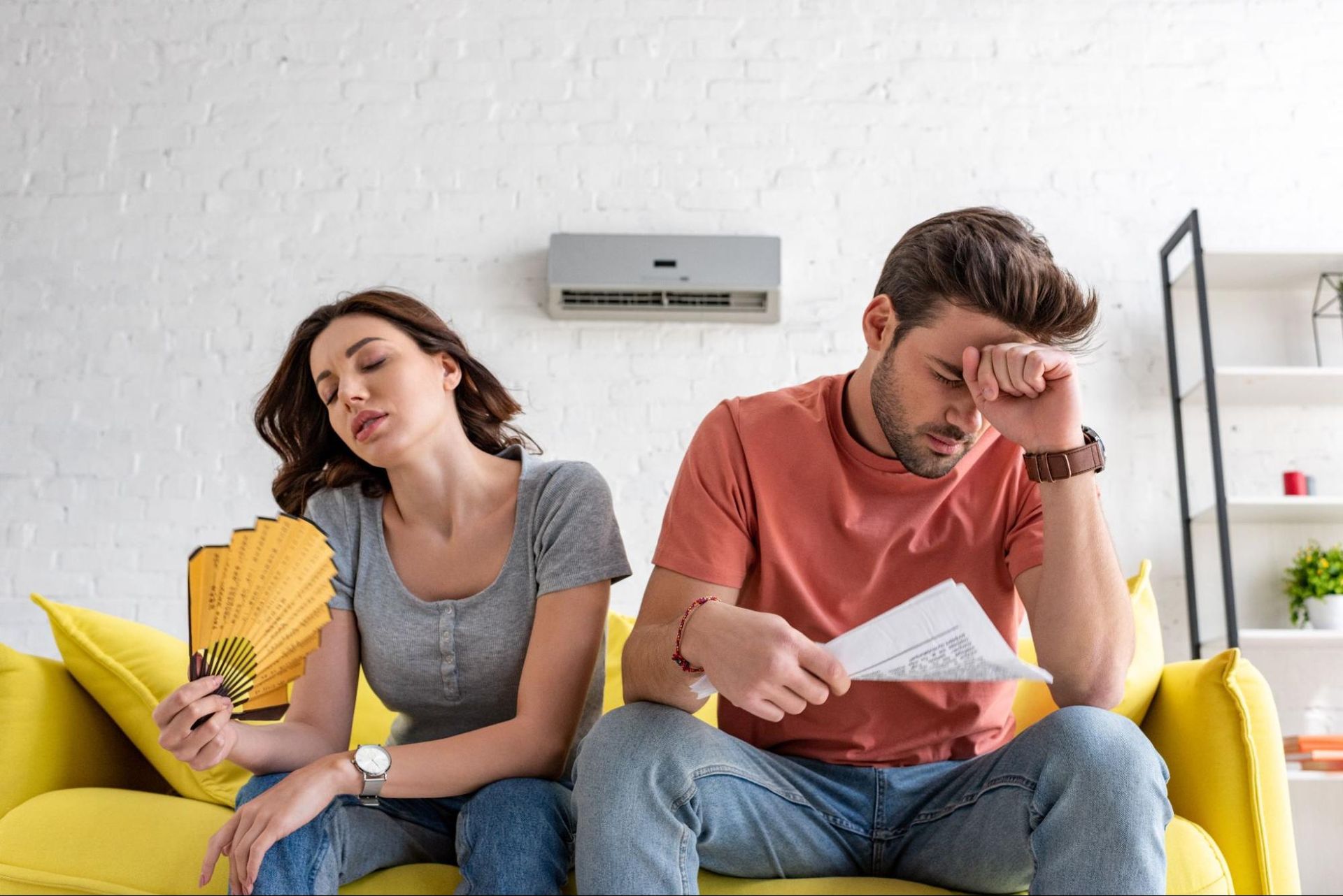 A man and a woman are sitting on a couch with a fan.