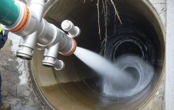 A pipe, installed by expert plumbers, discharges a strong stream of water into a large concrete drain, creating a swirling motion inside the tunnel.