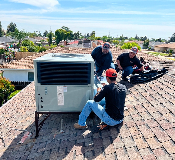 Three workers in red caps install or service an HVAC unit on a residential rooftop, ensuring expert indoor air quality in a suburban neighborhood under a clear sky.