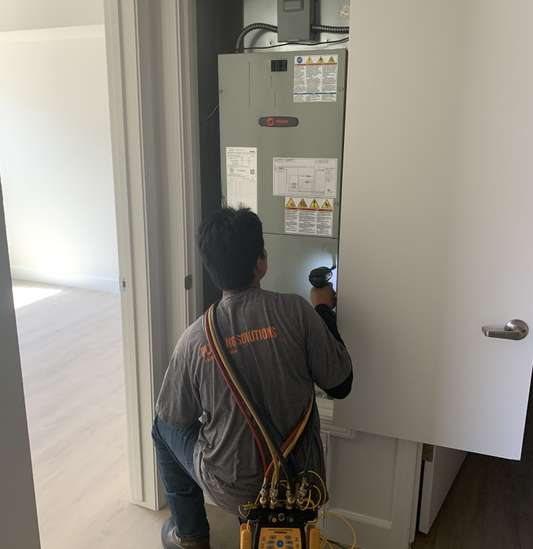 A technician uses a flashlight to inspect an HVAC unit inside a closet, with diagnostic tools hanging from their shoulder—essential steps during thorough heating maintenance.