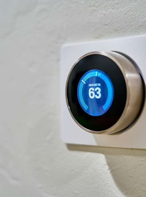 A smart thermostat mounted on a wall displays the heat set to 63 degrees, highlighting the comfort and efficiency delivered by quality heating services.
